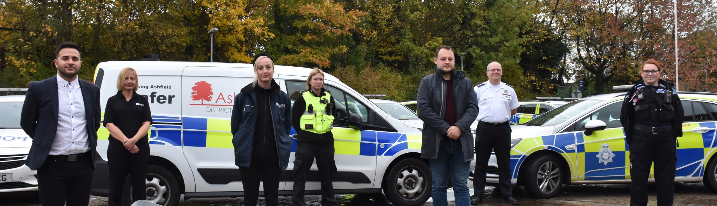 Council officers and a police officer pose in front of a police car outside 