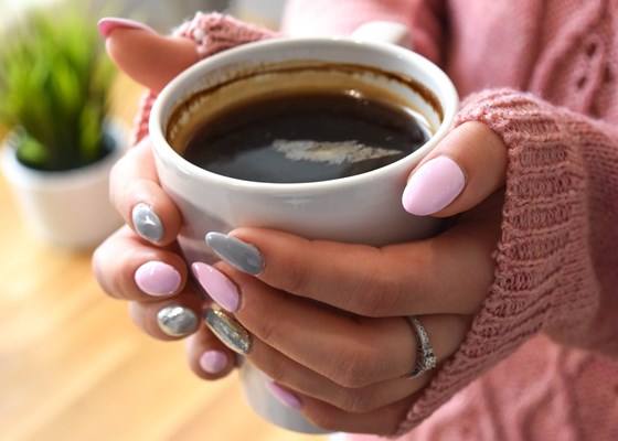 a full coffee cup of warm black coffee being held between 2 hands