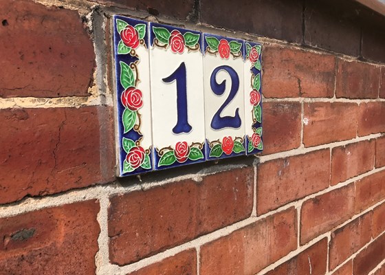 Decorative house number plaque on red brick wall - reading 12