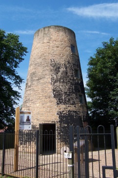 Lindley's Mill - stone tower shaped building with open doorway, behind railings with blue skies