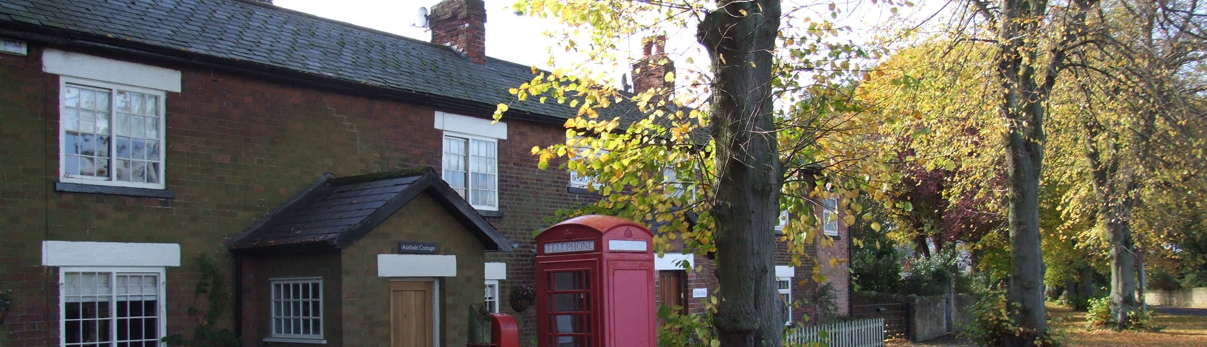 Row of brick cottages under trees with red phone box