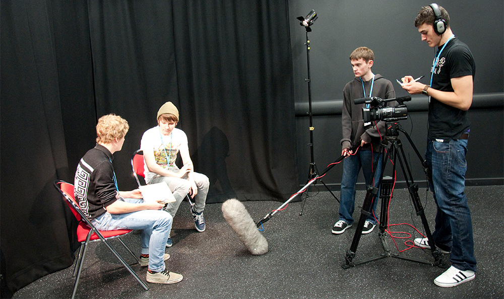 Students in a studio with TV and sound equipment filming an interview