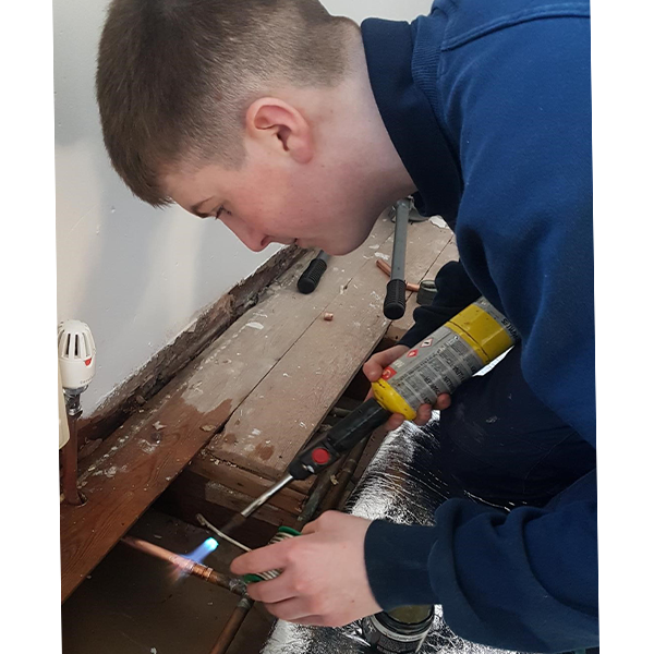 Young man bending over floorboards using a blow-torch to weld copper pipes