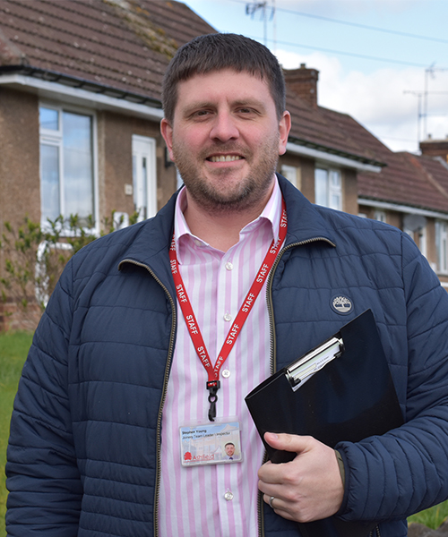 Man smiling at camera and wearing a work lanyard and carrying a clipboard