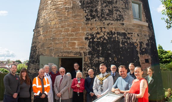 A group of people are stood in front of Lindley's Mill in Sutton 