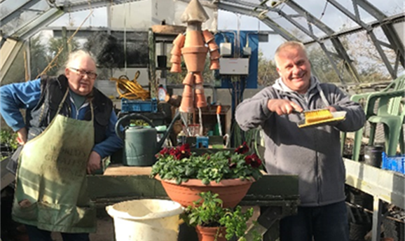 Two men in a greenhouse holding up plants