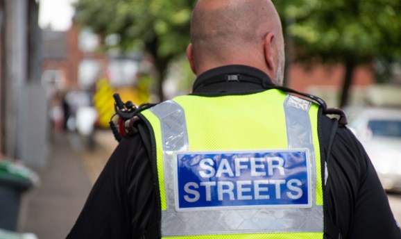 Police officer walking a street with hi viz vest with safer streets badge 