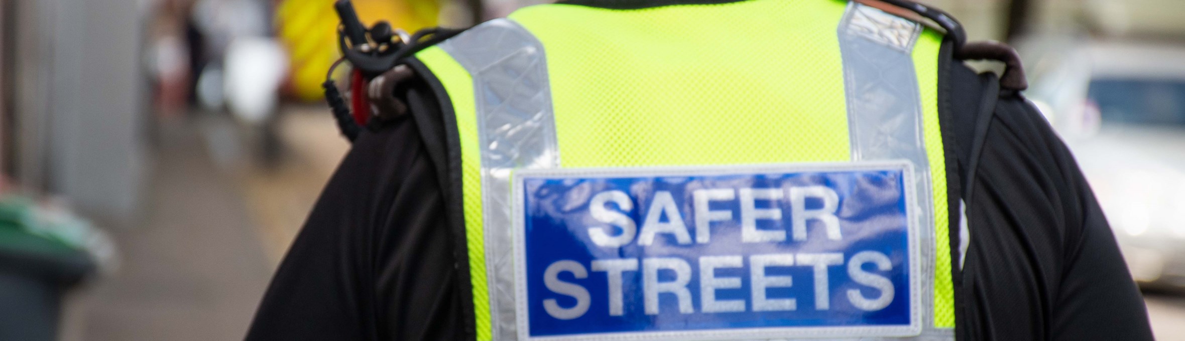 Police officer walking a street with hi viz vest with safer streets badge 