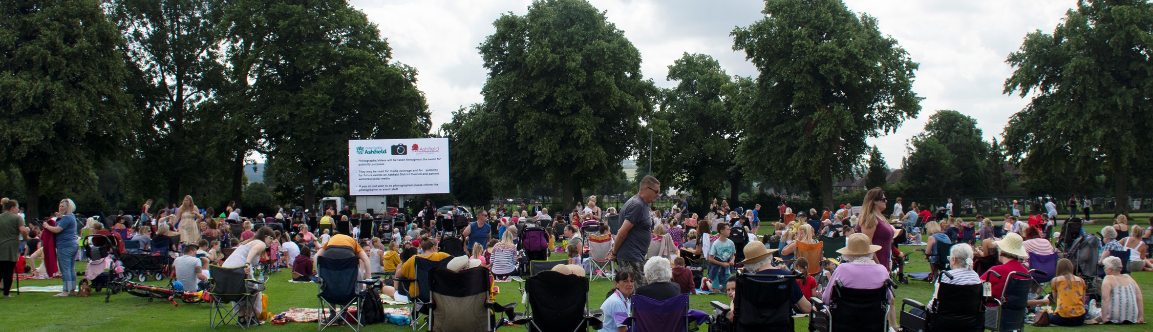 hundreds of people sitting on fold out chairs watching a big screen on Titchfield Park