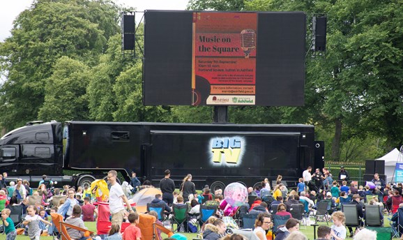 crowds of people sat in deck chairs in front of a giant screen on sutton lawn 