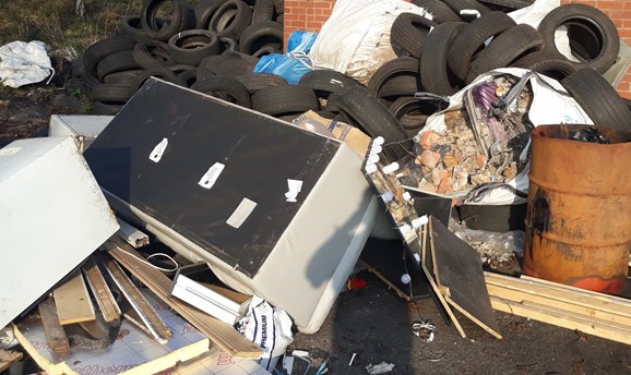 a large pile of flytipped rubbish including a sofa, hundreds of tyres and oil drums 
