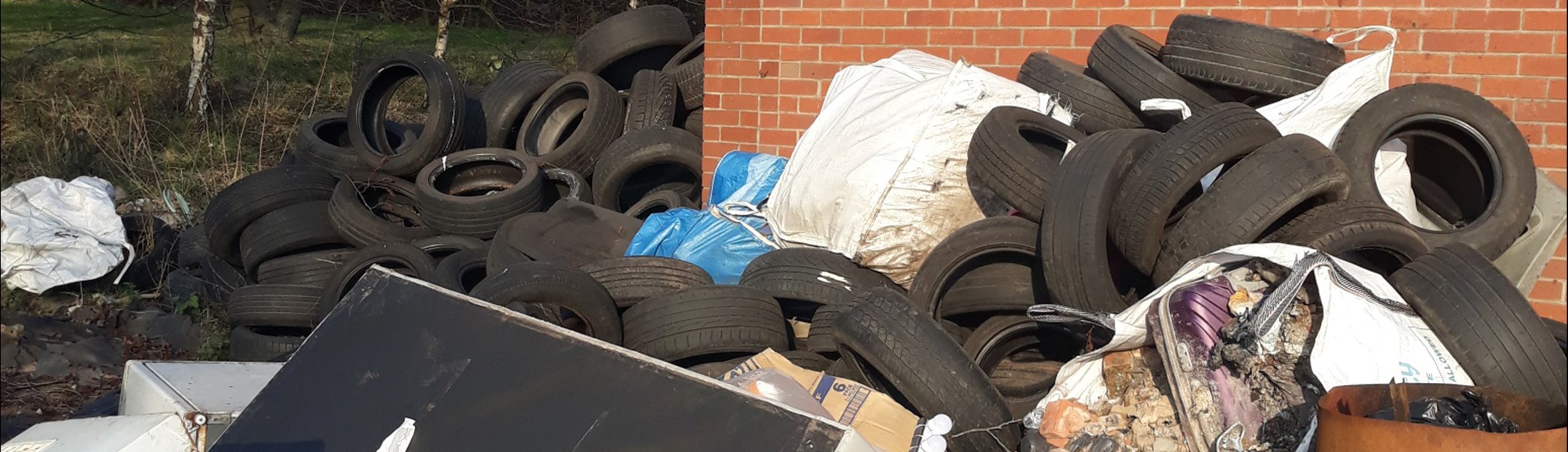 a large pile of flytipped rubbish including a sofa, hundreds of tyres and oil drums 