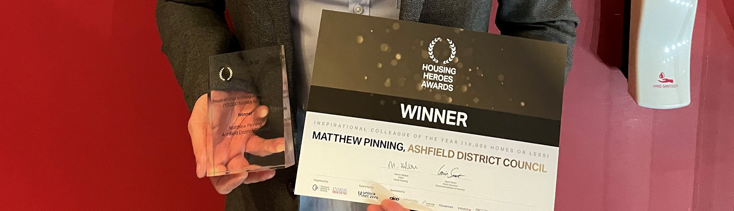 Matthew Pinning smiling holding his award in front of a red wall