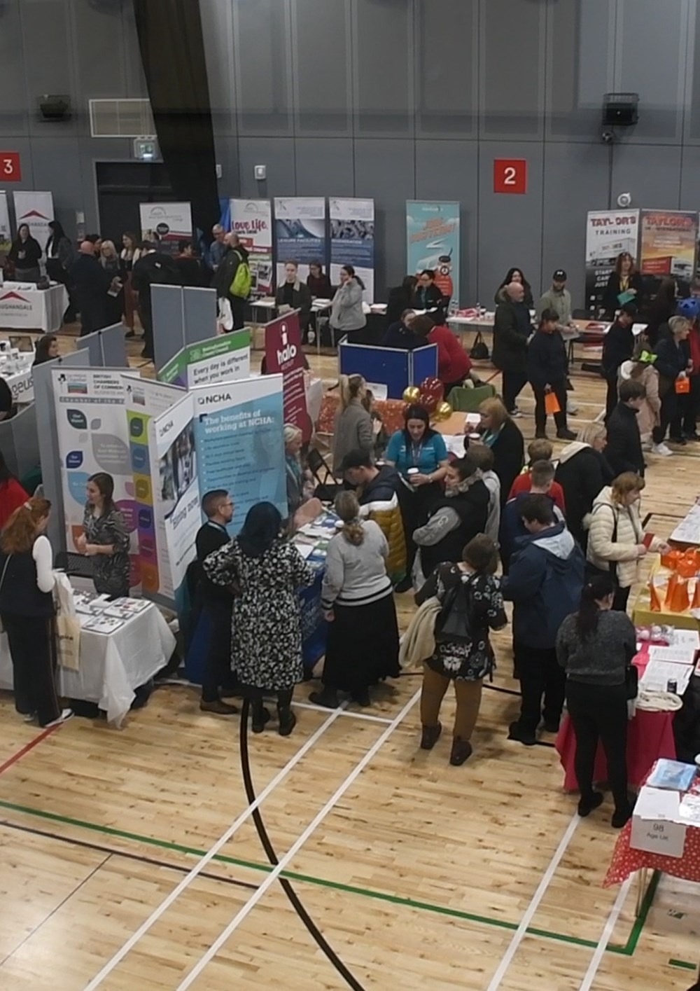 Stalls and people attending the last careers fair in a sports hall
